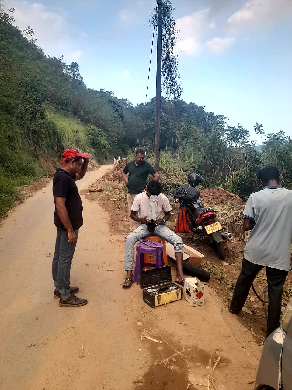 Dialog Axiata field technician using a mobile GIS device to locate a network asset on a hill road in Sri Lanka